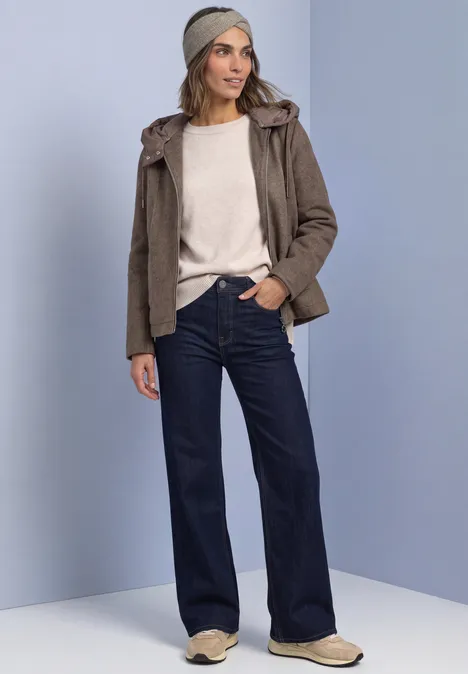 Stirnband in Melange-Optik Muddy Mocha Frau in Freizeitlook mit beigem Pullover, khakifarbener Jacke, weiten Jeans und beigen Schuhen.