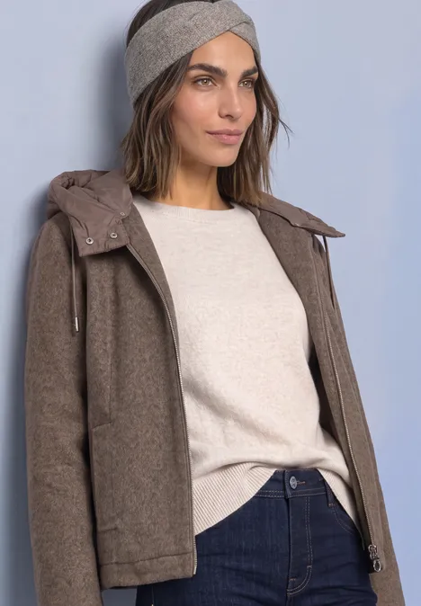 Stirnband in Melange-Optik Muddy Mocha Frau in brauner Jacke, beigem Pullover, Jeans und Stirnband vor hellem Hintergrund.