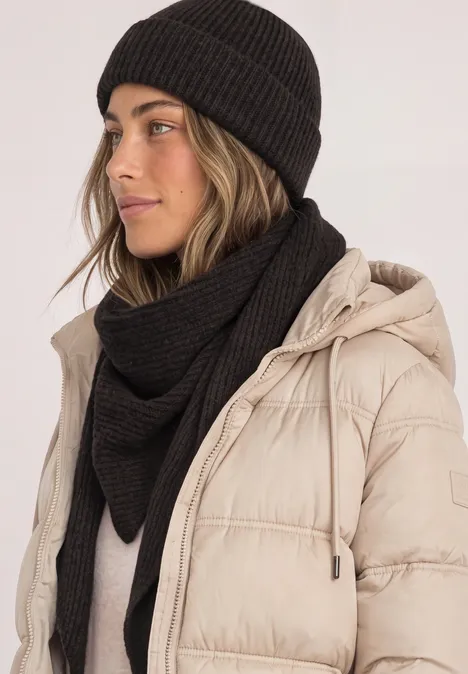 Frau mit schwarzer Strickmütze und passendem Schal trägt hellbeige gesteppte Winterjacke