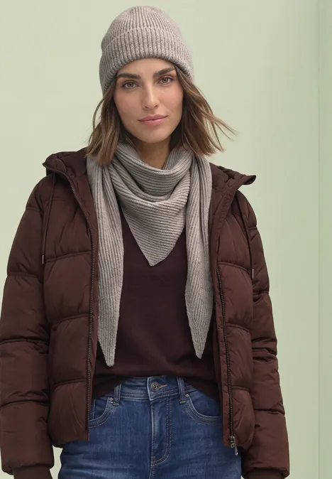 Beanie in Melange-Optik Muddy Mocha Frau in brauner Steppjacke, Jeans, grauem Schal und Mütze vor hellem Hintergrund.