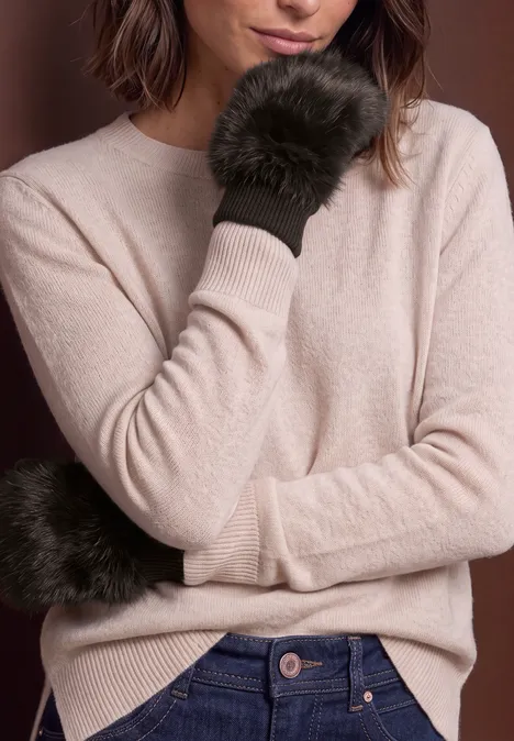 Vrouw in beige trui poseert met zwarte, pluizige wanten.