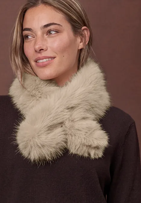 Effen stropdas van imitatiebont smooth stone sand Eine Frau mit einem hellen, flauschigen Kunstpelzschal und braunem Pullover vor schlichtem Hintergrund.