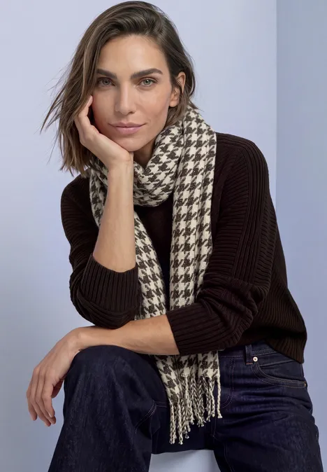 Écharpe à motif pied-de-poule et paillettes auburn brown Eine Frau in dunklem Pullover und Jeans mit Hahnentritt-Schal sitzt lässig, Hand an der Wange.