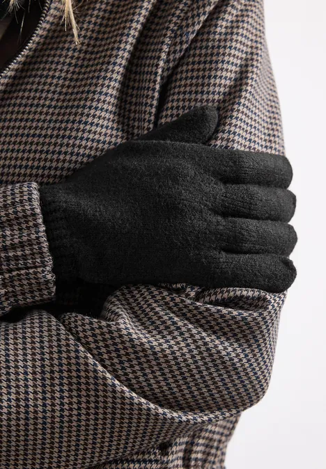 Feinstrick Handschuhe in Unifarbe Black Nahaufnahme: Person in Hahnentrittmantel mit schwarzen Handschuhen, die Arme verschränkt vor der Brust.