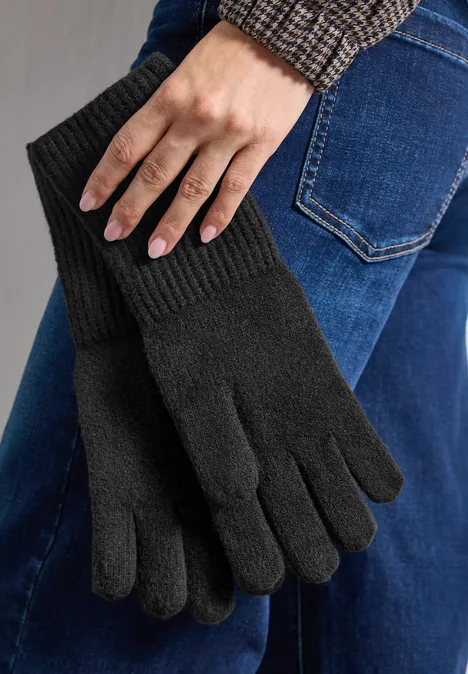 Feinstrick Handschuhe in Unifarbe Black Schwarze, gestrickte Fingerhandschuhe, von einer Hand vor Jeansgewebe gehalten.