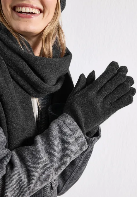 Feinstrick Handschuhe in Unifarbe anthracite melange Lächelnde Person mit grauem Schal, grauem Mantel und schwarzen Handschuhen vor weißem Hintergrund.