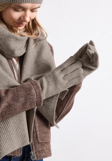 Frau in Winterbekleidung zieht graue Handschuhe an.