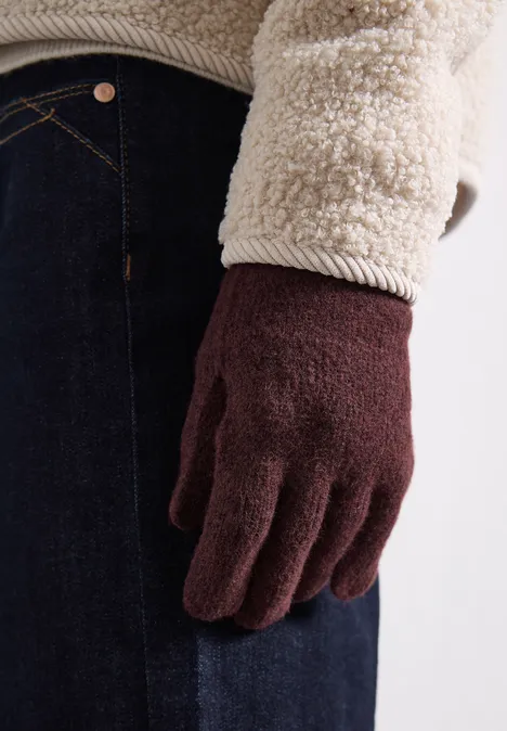 Eine Person trägt braune Strickhandschuhe und eine flauschige Fleecejacke.