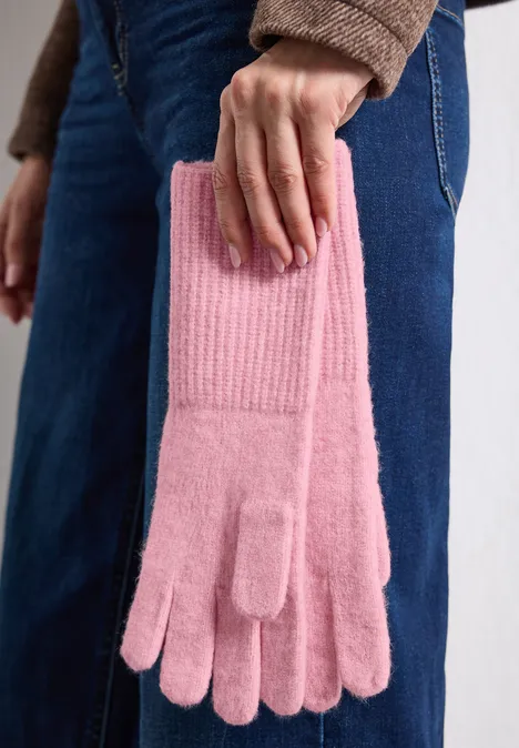 Een persoon in jeans houdt een paar roze gebreide handschoenen in de hand.