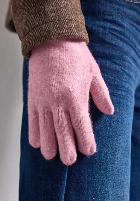Nahaufnahme einer Person mit pinkem Handschuh aus Fleece neben Jeans und brauner Jacke.