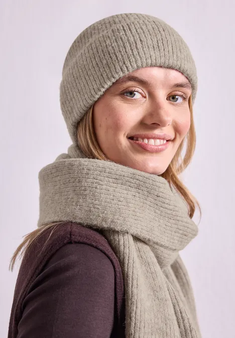 Lächelnde junge Frau trägt graue Strickmütze und passenden Schal.