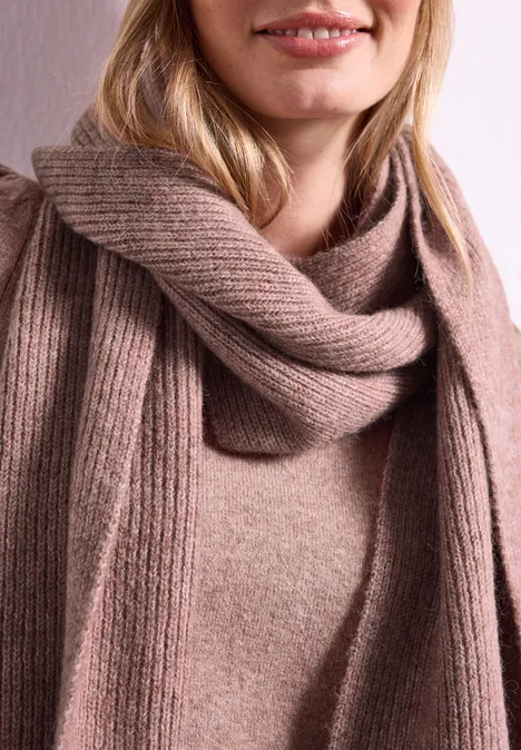 Beige gestrickter Schal und Pullover an einer lächelnden Frau, Fokus auf Oberkörper.