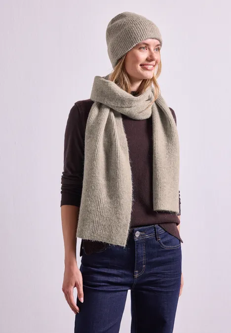 Junge Frau in beiger Mütze und passendem Schal, dunklem Pullover und Jeans.