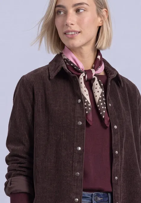 Doek met grafisch patroon rustic rouge Frau mit blondem Bob trägt braune Cordjacke, weinrotes Shirt und gepunktetes lila Halstuch, schaut seitlich.