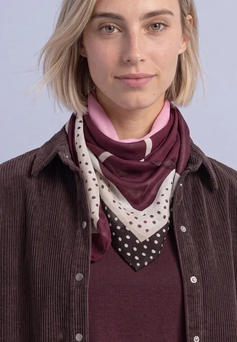 Doek met grafisch patroon rustic rouge Frau mit blondem Bob trägt braune Cordjacke, weinrotes Shirt und gemustertes Halstuch vor hellem Hintergrund.
