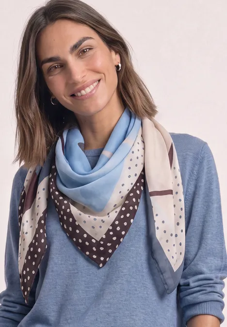 Lächelnde Frau in blauem Pullover und gemustertem Dreieckstuch.