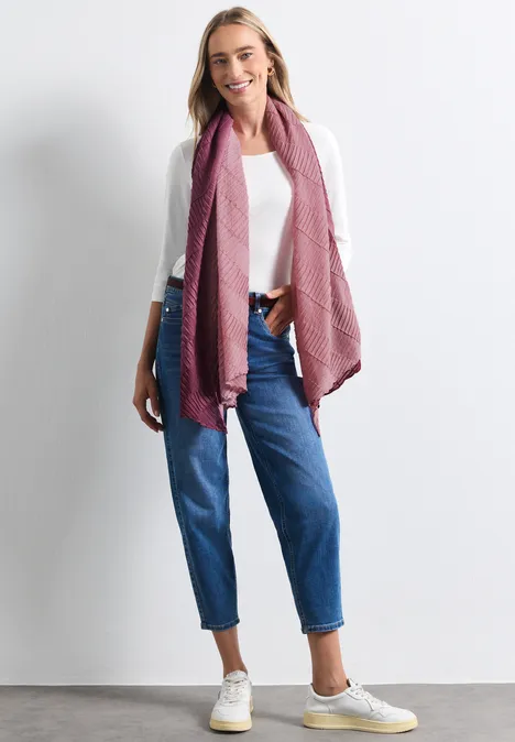 Lange sjaal met kleurverloop rustic rouge Frau lächelnd in weißem Shirt, blauen Jeans und rosa Schal vor weißem Hintergrund.