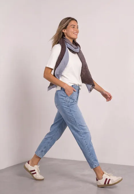 Lange sjaal met kleurverloop northern blue Frau spaziert fröhlich in Jeans, weißem T-Shirt, Sneakern und Schal vor schlichtem Hintergrund.