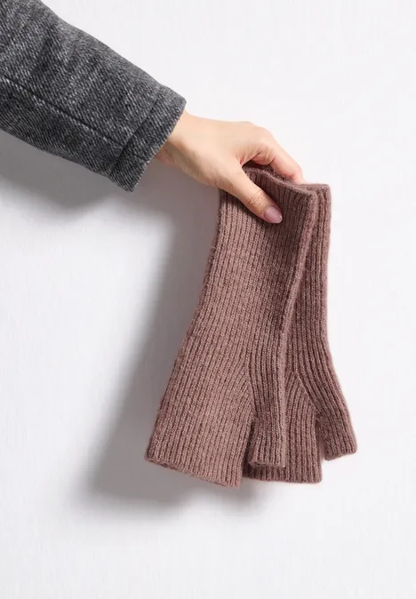 Eine Hand hält ein Paar brauner, gestrickter fingerloser Handschuhe vor einer hellen Wand.