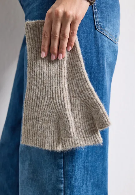 Hand hält beigefarbenen, gerippten Strickschal vor blauen Jeans