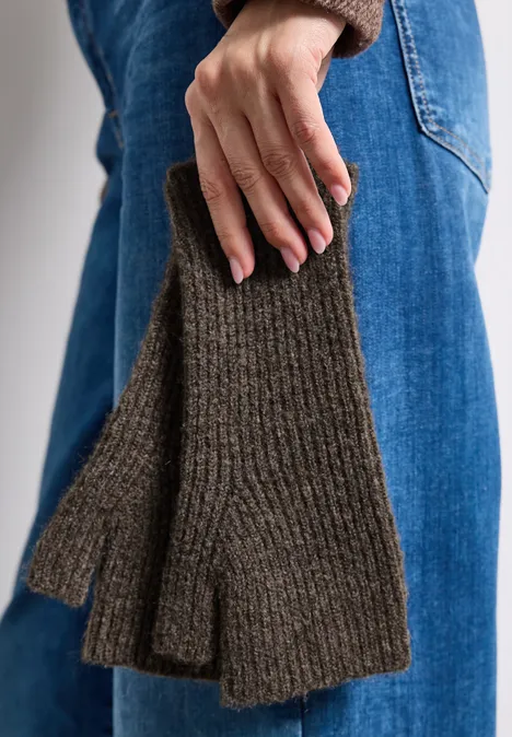 Nahaufnahme einer Person in Jeans, die olivgrüne, gestrickte Fingerhandschuhe trägt.
