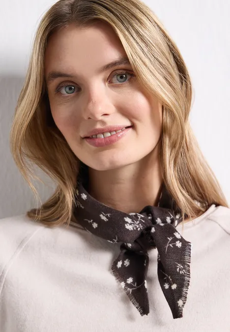 Junge Frau mit blondem Haar trägt helles Oberteil und geblümtes Halstuch, sie lächelt leicht ins Bild.