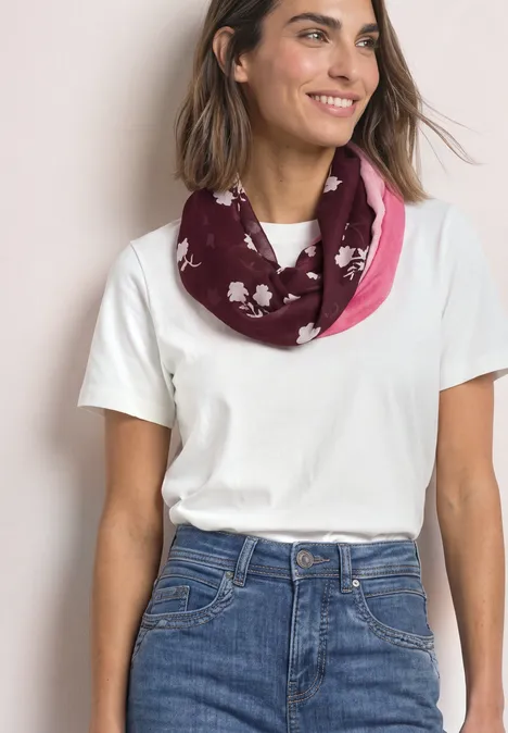 Loop-Schal mit floralem Muster rustic rouge Frau in weißem T-Shirt und Jeans trägt einen rosa-bordeauxfarbenen Loop-Schal mit weißen Blumenmustern.