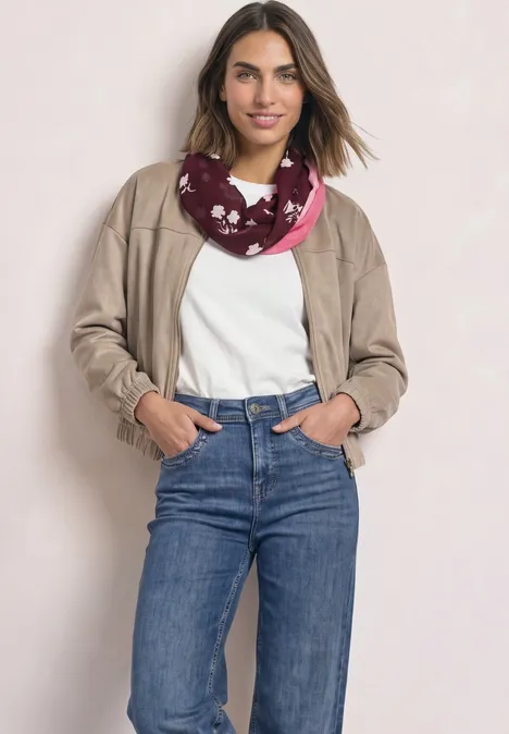 Loop-Schal mit floralem Muster rustic rouge Eine Frau in casual Outfit mit beiger Jacke, weißem Shirt, blauen Jeans und rosarotem Schal mit Muster.