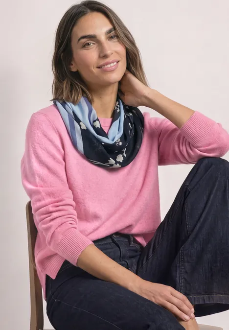 Loop-Schal mit floralem Muster indigo night Frau in rosa Pullover und gemustertem Halstuch sitzt lässig auf einem Stuhl und lächelt leicht.
