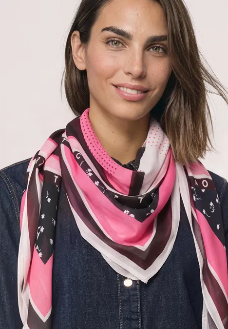 Quadratisches Tuch mit Grafikprint multicolor Porträt einer Frau mit braunen Haaren, die ein pink-weiß-schwarzes Tuch um den Hals trägt.