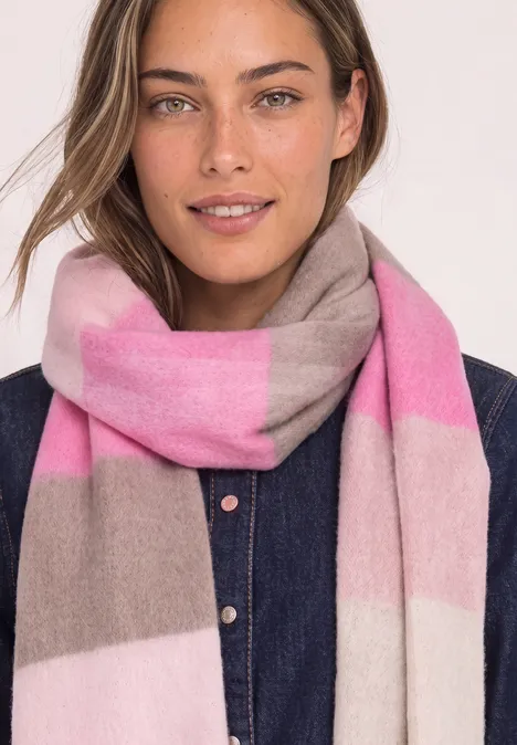 Femme portant une écharpe rose et grise, souriante devant un fond clair.