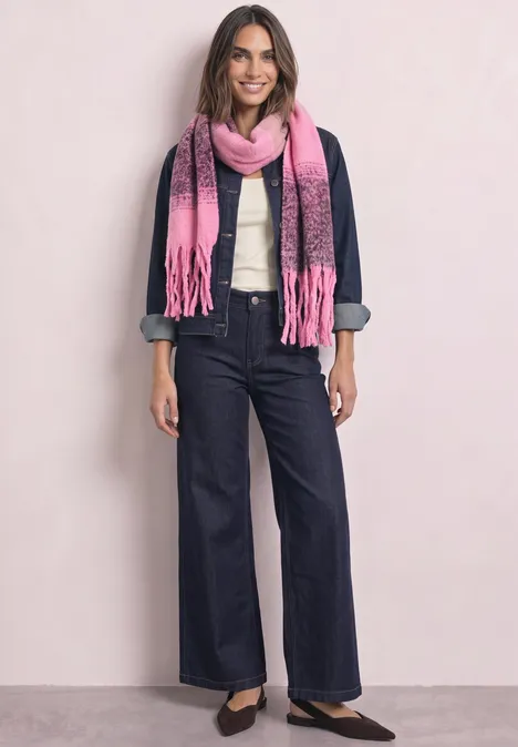 Femme souriante en veste en jean, chemise blanche, jean large, écharpe rose et ballerines noires sur fond clair.