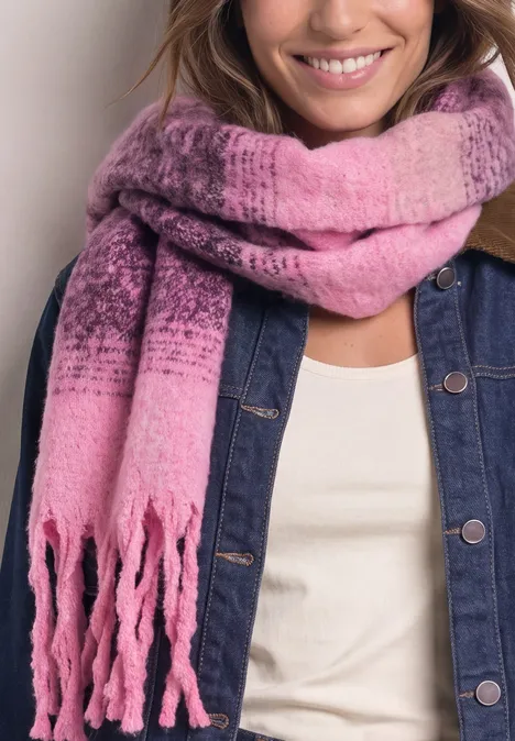 Femme souriante porte une écharpe dégradée rose à franges sur une veste en jean et haut blanc.