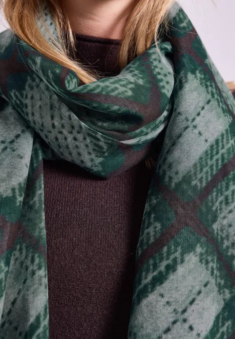 Eine Frau trägt einen grünen, karierten Schal über einem braunen Pullover.