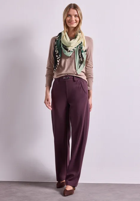 Quadratisches Tuch mit Grafikprint multicolor Frau vor hellem Hintergrund trägt beigen Pullover, gemusterten Schal, weinrote Marlenehose und braune Loafer.