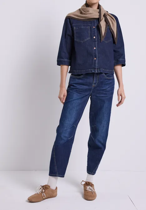 Een persoon draagt een donkerblauwe spijkerblouse, jeans, een sjaal en bruine veterschoenen.