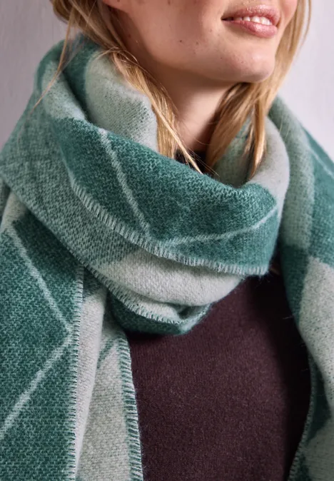Frau trägt weichen, karierter grüner Schal über einem dunklen Pullover, Nahaufnahme von Hals und Schultern.