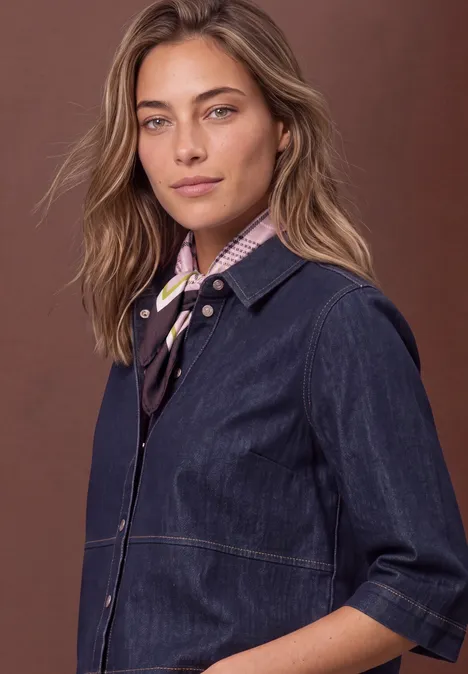 Foulard avec un effet satiné à carreaux multicolor Eine Frau mit langen braunen Haaren trägt eine dunkelblaue Jeansjacke und ein buntes Halstuch vor braunem Hintergrund.