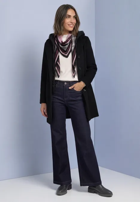 Sjaal met argyle-patroon berry plum Frau in schwarzer Jacke, helles Oberteil, Schal und weiten Jeans, steht lächelnd vor hellem Hintergrund.