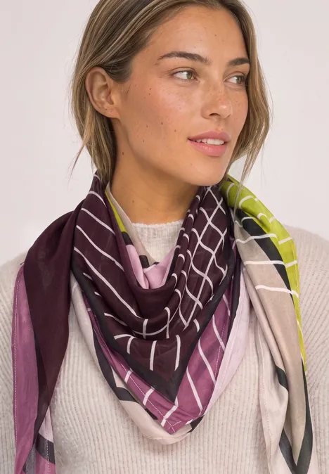Doek met grafisch patroon multicolor Frau trägt eleganten Schal mit geometrischem Muster in Lila, Grün und Beige.