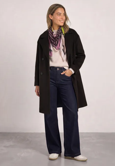 Doek met grafisch patroon multicolor Frau in schwarzem Mantel, weißem Pullover, weiten Jeans, weißen Schuhen und gemustertem Schal.