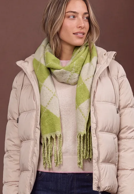 Frau in heller Daunenjacke und grün-grauem Karoschal, seitlich in die Ferne schauend.