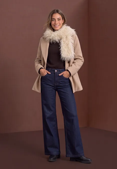 Schal aus Fake Fur in Unifarbe clay sand Frau in hellbraunem Mantel mit Fellkragen, braunem Pullover, hochgeschnittener Schlagjeans und schwarzen Stiefeletten.