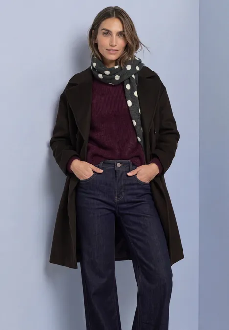 Longue écharpe à motifs de pois armor grey mel. Frau in schwarzem Mantel, gepunktetem Schal, weinrotem Pullover und dunkler Jeans vor hellem Hintergrund.