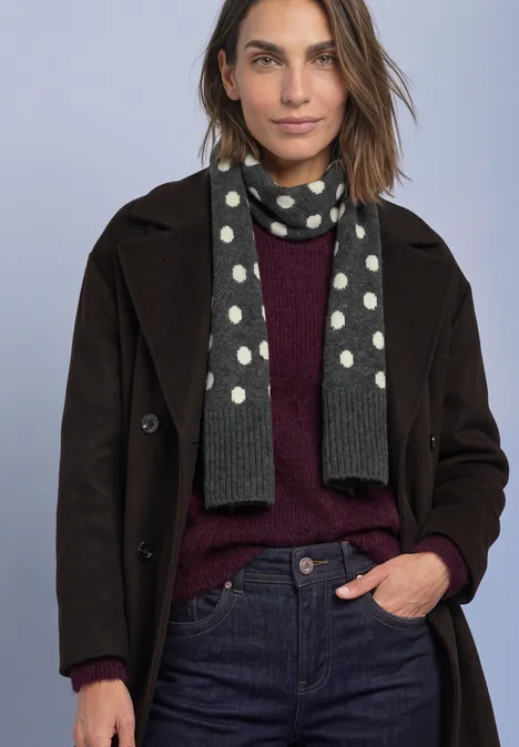 Longue écharpe à motifs de pois armor grey mel. Frau in dunkelbraunem Mantel, weinrotem Pullover, Jeans und grauem Schal mit weißen Punkten.