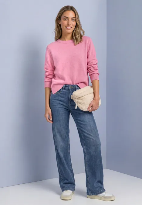 Teddy-Umhängetasche in Unifarbe barley beige Eine Frau trägt rosa Pullover, weite Jeans, weiße Sneaker und hält eine beige Gürteltasche vor hellgrauer Wand.