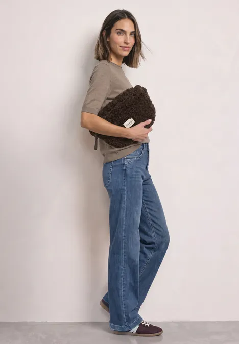 Teddy-schoudertas in effen kleur auburn brown Vrouw in profiel met een bruine pluche tas, draagt een taupekleurige top, wijde jeans en bordeaux sneakers.