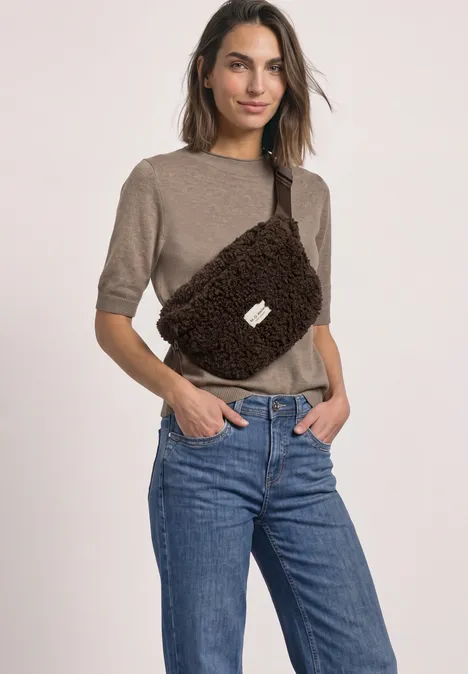 Teddy-schoudertas in effen kleur auburn brown Een vrouw draagt een beige kortmouwtrui, blauwe jeans en een bruine pluizige heuptas voor een neutrale achtergrond.