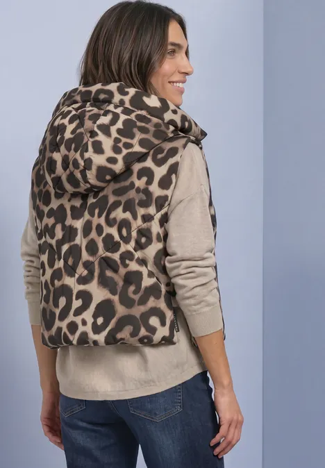 Vrouw gezien van achter in een gewatteerd capuchonvest met luipaardprint, beige trui en jeans.
