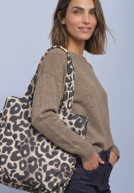 Eine Frau trägt einen braunen Pullover, eine dunkelblaue Hose und eine große Leoparden-Print-Tasche.